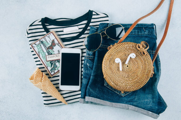 Summer women's clothing and accessories flat lay, featuring denim shorts, striped shirt, sunglasses, and straw